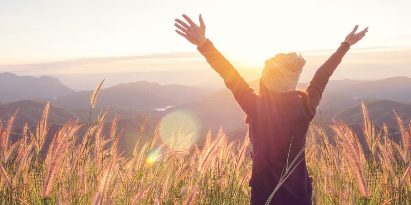 girl with hands up in field near mountains