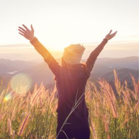 girl with hands up in field near mountains
